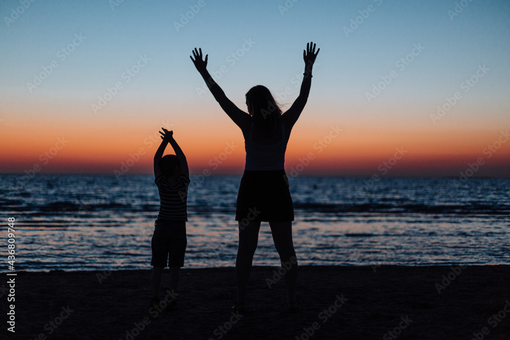 Silhouette of mother and son. Stand on the beach, against the backdrop of the sunset on the sea
