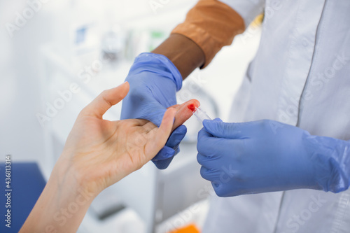Wall Mural Unrecognizable female African American health worker doing a finger prick test for HIV, drawing blood into a test tube after pricking the patient with a scarifier