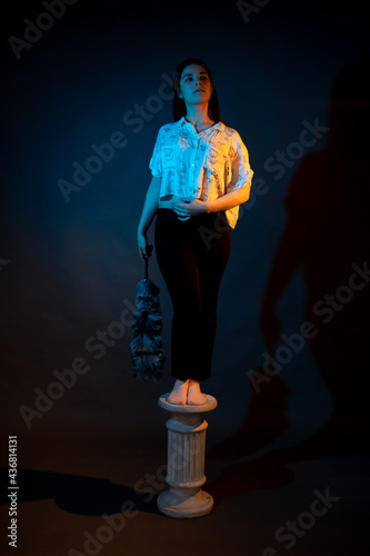 A girl stands on a miniature Greek column illuminated by multicolored light