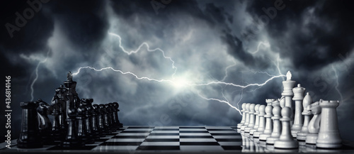 Billede på lærred Chess pieces on a chessboard against the backdrop of a stormy sky and flashing lightning