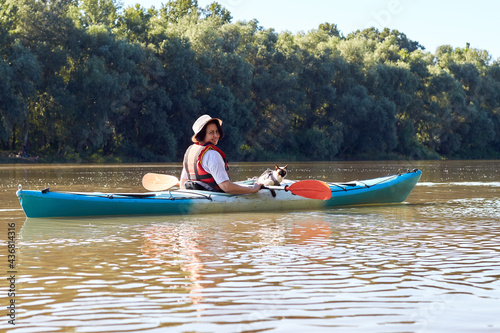 Woman rowing a blue kayak with her mekong bobtail (siames) cat at the river. Domestic lying on a kayak on the kayak © watcherfox