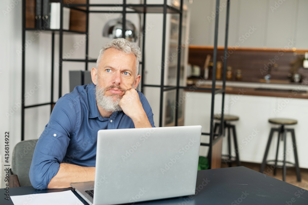 Pensive mature man solving difficult business task sitting at the desk with a laptop and looks away, senior male entrepreneur thinking Pensive mature man solving difficult business task sitting at the desk with a laptop and looks away, senior male entrepreneur thinking