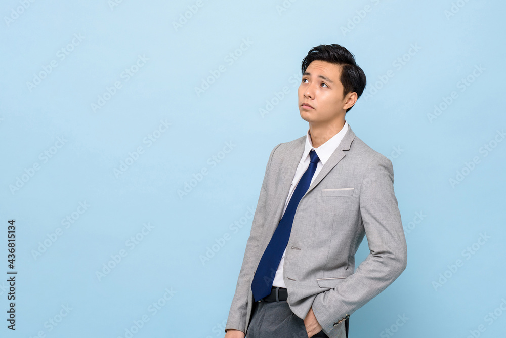 Bored Asian businessman thinking and looking up to copy space aside in isolated light blues studio background Bored Asian businessman thinking and looking up to copy space aside in isolated light blues studio background