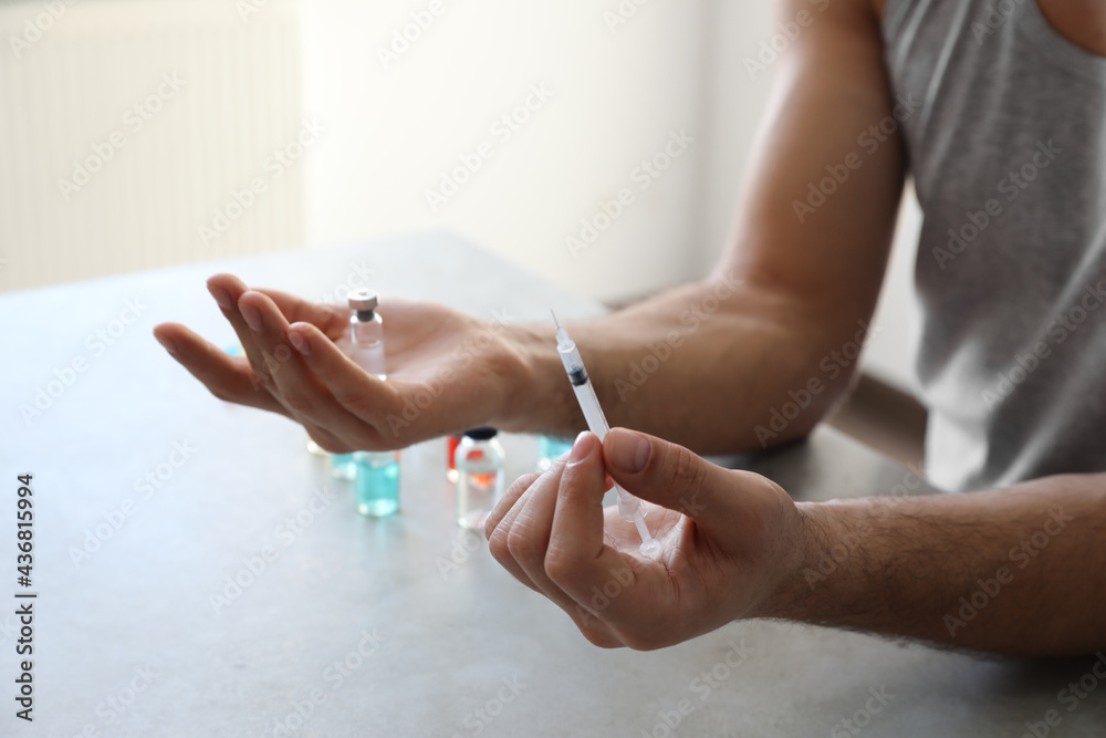 Man with syringe and vial at grey table, closeup. Doping concept