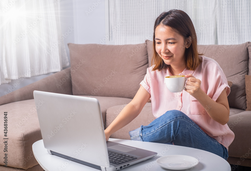bussiness woman or student sitting on sofa in living room drinking coffee or tea looking at the compoter notebook or laptop. Stay and Work from home and student study and learn online at home office. bussiness woman or student sitting on sofa in living room drinking coffee or tea looking at the compoter notebook or laptop. Stay and Work from home and student study and learn online at home office.