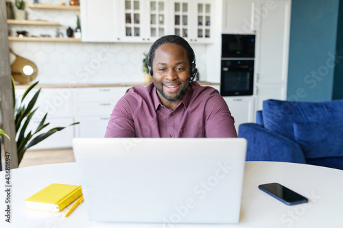 Guy in wirelessheadset using laptop sitting in the kitchen home. Remote work concept photo