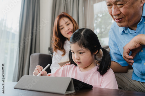 Asian grandparents and granddaughter video call at home. Senior Chinese, grandpa and grandma happy with girl using mobile phone video call talking with dad and mom lying in living room at home.