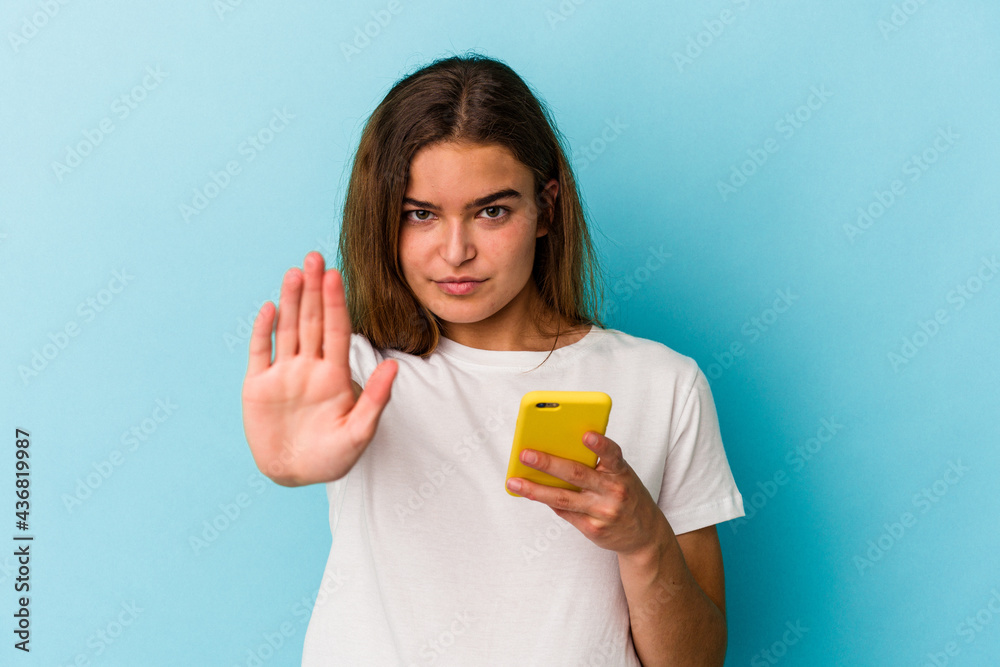 Young caucasian woman holding a mobile phone isolated on blue background standing with outstretched hand showing stop sign, preventing you. Young caucasian woman holding a mobile phone isolated on blue background standing with outstretched hand showing stop sign, preventing you.