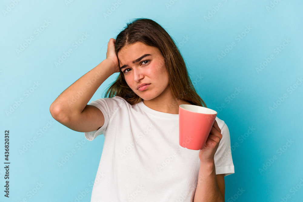 Young caucasian woman holding a mug isolated on blue background being shocked, she has remembered important meeting. Young caucasian woman holding a mug isolated on blue background being shocked, she has remembered important meeting.