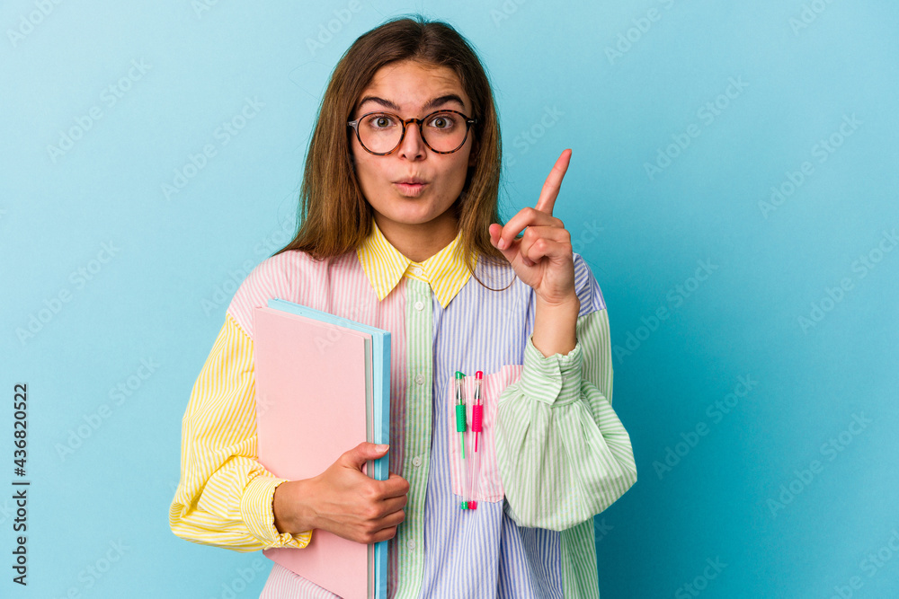 Young caucasian student woman holding books isolated on blue background having some great idea, concept of creativity. Young caucasian student woman holding books isolated on blue background having some great idea, concept of creativity.