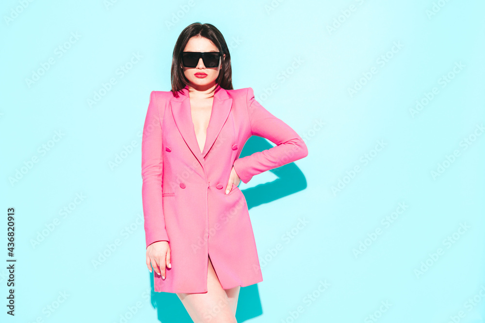 High fashion portrait of young beautiful brunette woman wearing nice pink summer suit.Sexy trendy model posing near blue wall in studio.Fashionable female in sunglasses High fashion portrait of young beautiful brunette woman wearing nice pink summer suit.Sexy trendy model posing near blue wall in studio.Fashionable female in sunglasses