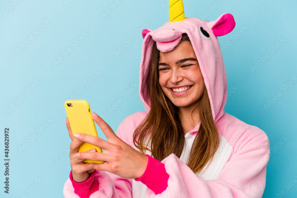 Young caucasian woman wearing a unicorn pajama holding a mobile phone isolated on blue background Young caucasian woman wearing a unicorn pajama holding a mobile phone isolated on blue background