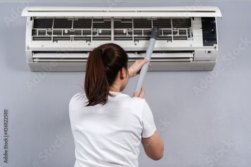 woman using vacuum cleaner to cleaning the air conditioner at home