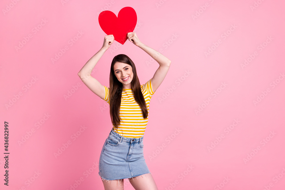 Photo of friendly millennial lady hold heart up wear orange t-shirt skirt isolated on pastel pink color background Photo of friendly millennial lady hold heart up wear orange t-shirt skirt isolated on pastel pink color background