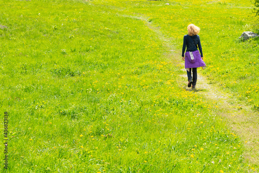 Woman walking alone on a path in a green meadow, with yellow flowers. Useful concept for freedom, free, lonely, loneliness. With copy-space.