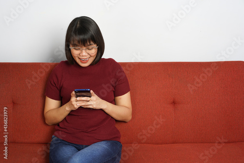 Using smartphone of Young beautiful Asian women dress red shirt and jeans sitting on red couch