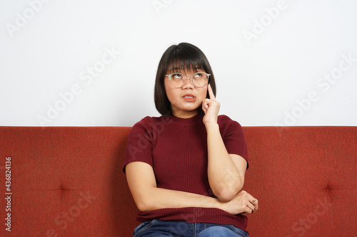 Thinking gesture Young beautiful Asian women dress red shirt and jeans sitting on red couch