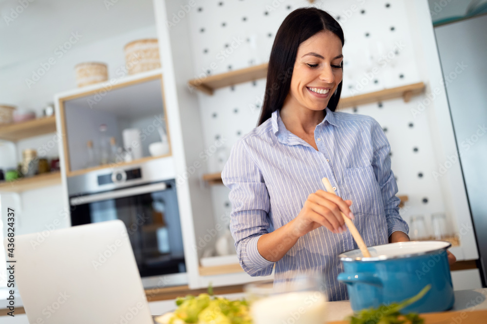 Happy woman in kitchen following recipe on digital device during cooking. Happy woman in kitchen following recipe on digital device during cooking.
