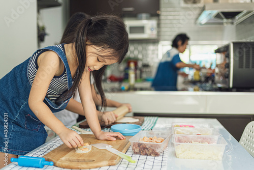 Asian in casual dress having fun while make pizza with prosciutto, tomato, cheese, vegetables in home kitchen. family and relationship concept