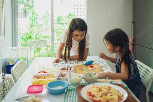 Asian in casual dress having fun while make pizza with prosciutto, tomato, cheese, vegetables in home kitchen. family and relationship concept