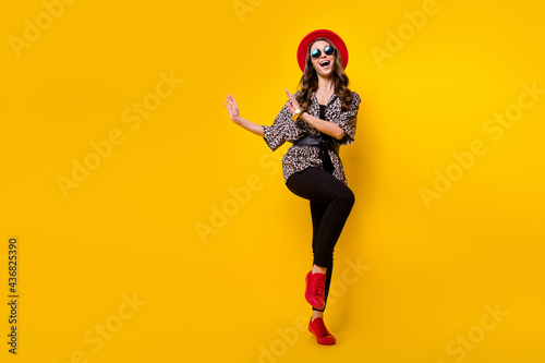 Full body photo of charming happy nice young woman wear red hat shoes dance copyspace isolated on yellow color background