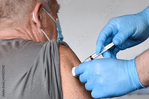 Elderly Man in Face Mask getting Covid Vaccine. Doctor giving Injection to senior Man at Hospital. Virus, COVID-2019, Flu protection. Vaccination of old Patient in Clinic during Coronavirus pandemic.