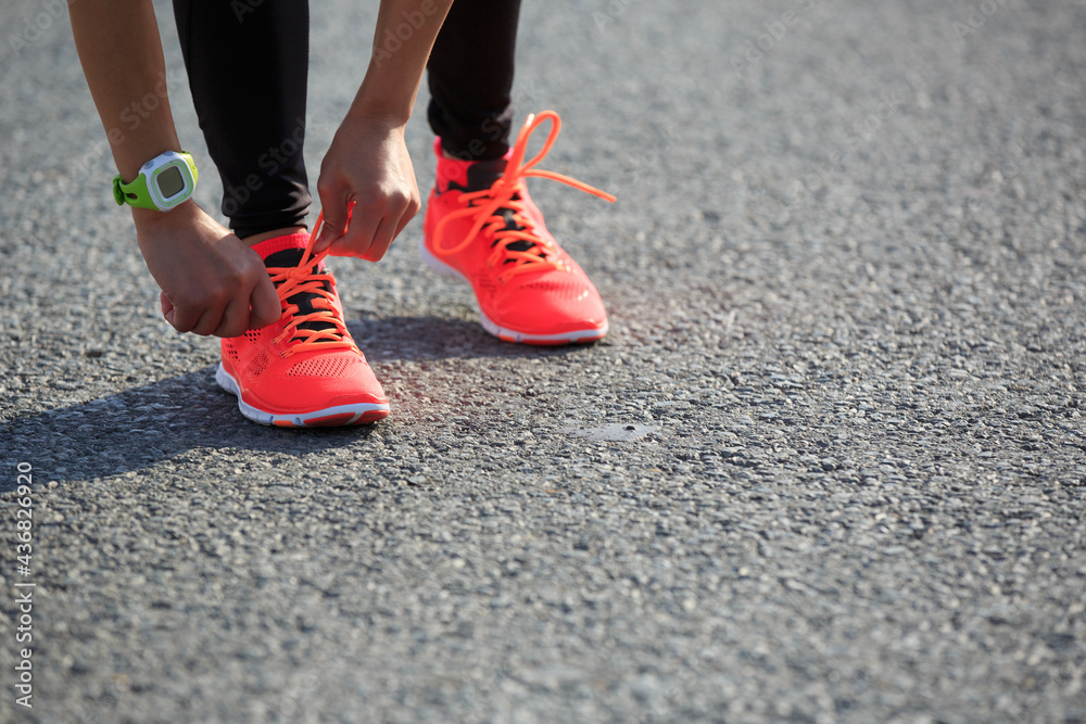 Young fitness woman runner tying shoelace on road