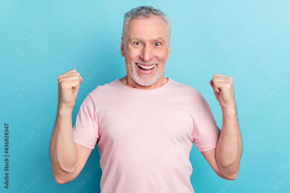 Photo portrait smiling elder man in pink t-shirt gesturing like winner isolated on pastel blue color background Photo portrait smiling elder man in pink t-shirt gesturing like winner isolated on pastel blue color background