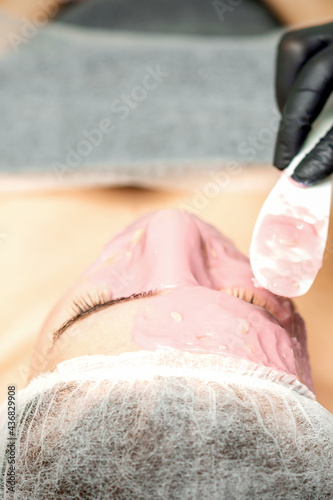 The cosmetologist applying an alginic mask to the face of a young woman in a beauty salon photo