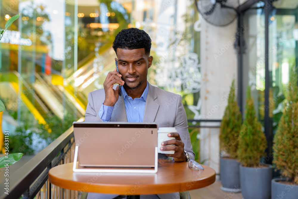 African businessman at coffee shop using laptop computer and talking on phone African businessman at coffee shop using laptop computer and talking on phone