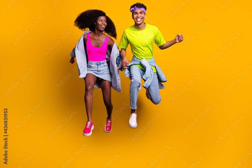 Full length body size view of handsome beautiful trendy cheery couple jumping holding hands isolated on bright yellow color background