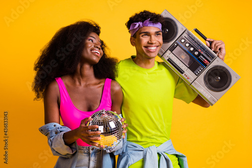 Photo of funky pretty young couple dressed denim outfit dancing holding boom box disco ball isolated yellow color background