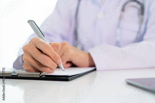 Doctor with a clipboard wrote on paper at the desk in the office.