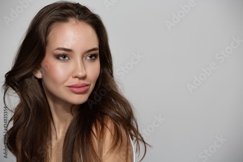 Portrait of beautiful young woman with natural skin make-up and brown hair on gray background