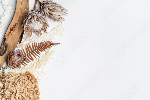 Rustic dried flower arrangement of pink King Protea, white Ruscus, orange Hydrangea, cream Amaranthus, rust fern leaf and decorative bark. Photographed from above, on a white background.