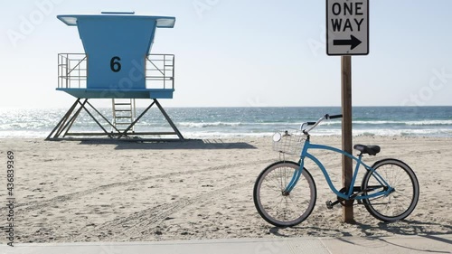 Blue bicycle, cruiser bike by sandy ocean beach, pacific coast, Oceanside California USA. Summertime vacations, sea shore. Vintage cycle by road sign One Way. Lifeguard tower, rescue watchtower hut.