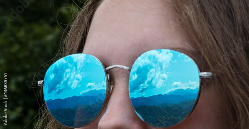 Close up image of reflection of mountains in mirror sunglasses on female's face. Creative image of showing beautiful nature and grea travel motivation photo