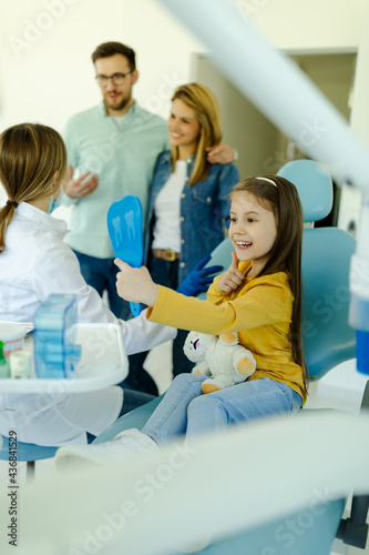 Girl looking in the mirror after dental procedure while parents standing near her for support.