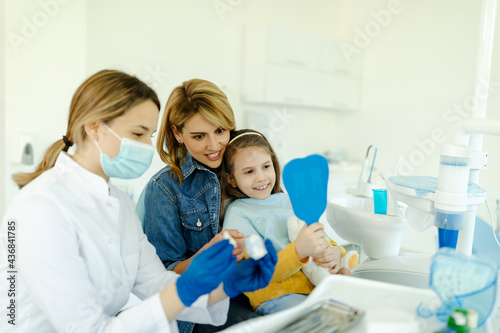Girl looking in the mirror after dental procedure while doctor is holding prosthesis.