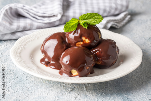 Delicious profiteroles with chocolate and white plate. Selective focus image on light background.