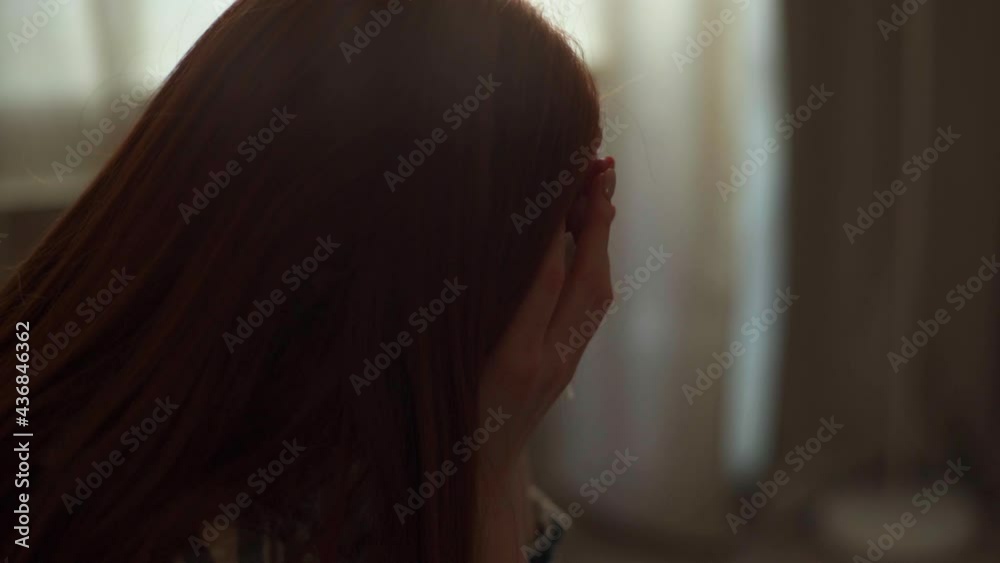 Close-up face of depressed young woman crying and wiping away tears with napkin sitting on bed in dark bedroom on background of window. Side view of sad female with broken relationship at home. Close-up face of depressed young woman crying and wiping away tears with napkin sitting on bed in dark bedroom on background of window. Side view of sad female with broken relationship at home.