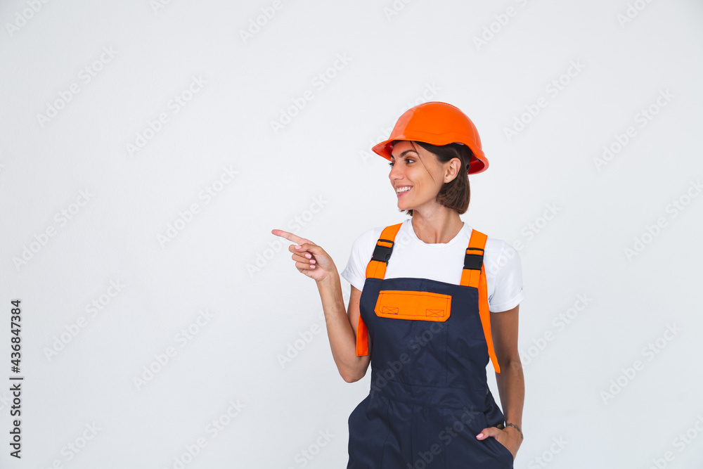 Pretty woman engineer in building protective helmet on white background confident smile point finger left Pretty woman engineer in building protective helmet on white background confident smile point finger left