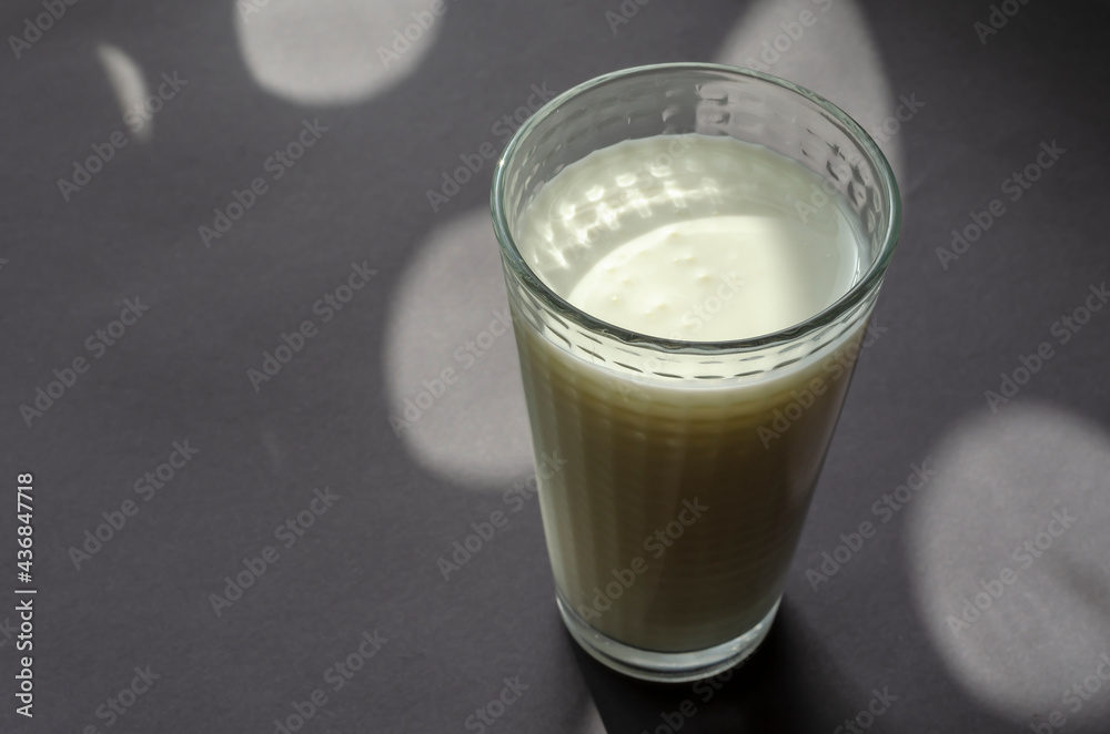 A glass of kefir on a gray surface with shadows.