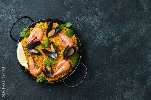 Traditional spanish seafood paella in pan with chickpeas, shrimps, mussels, squid on black concrete background. Top view with copy space