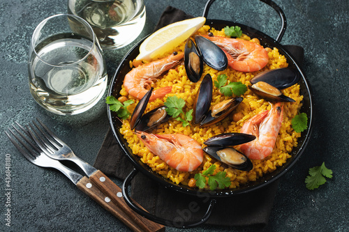 Traditional spanish seafood paella in pan with chickpeas, shrimps, mussels, squid on black concrete background. Top view