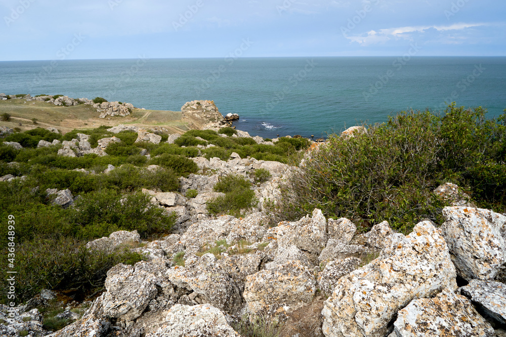 Sea view from the shore with large stones, green grass in summer.