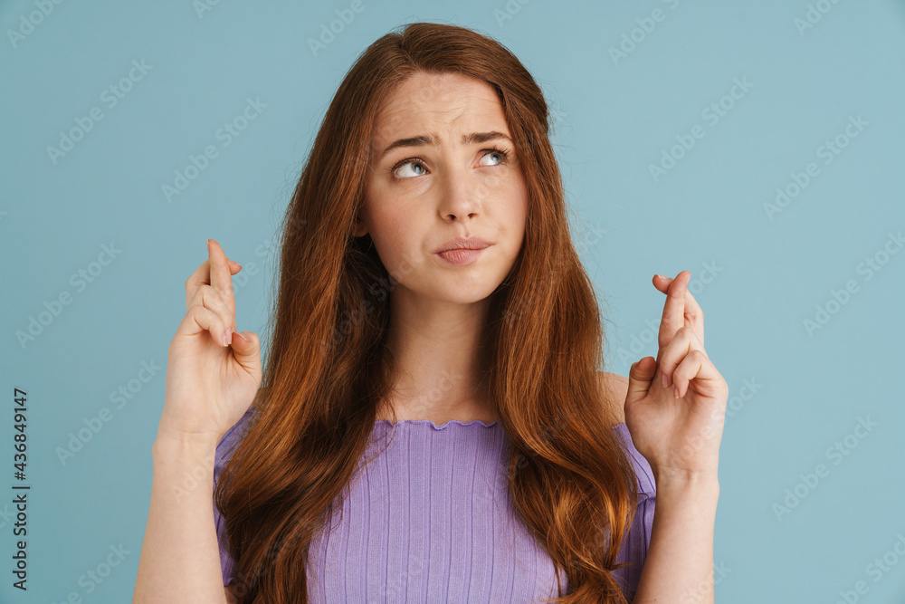 Young ginger woman frowning while holding fingers crossed for god luck Young ginger woman frowning while holding fingers crossed for god luck