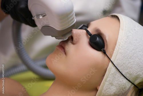 Therapist beautician makes a laser treatment to young woman's fa