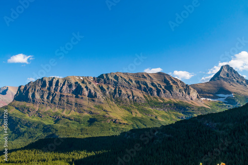 partially snow covered jagged mountain peaks of Glacier National park near Iceberg Lake trail during summer.