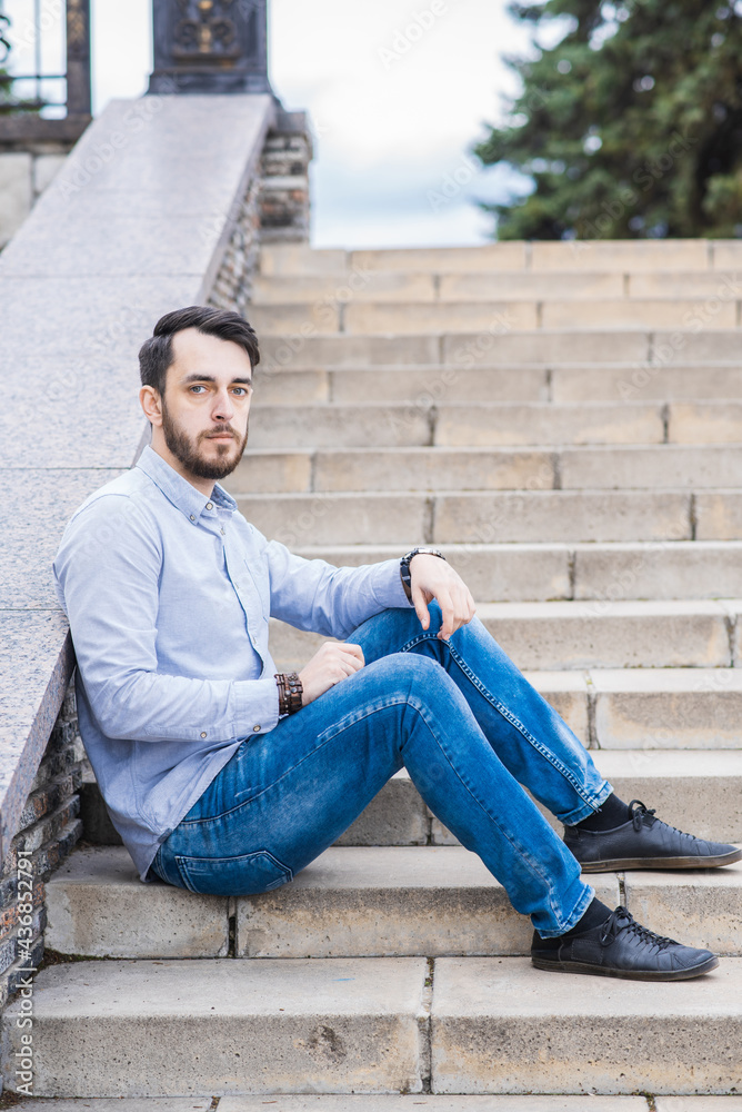 Portrait of a man businessman with a beard who sits on the steps